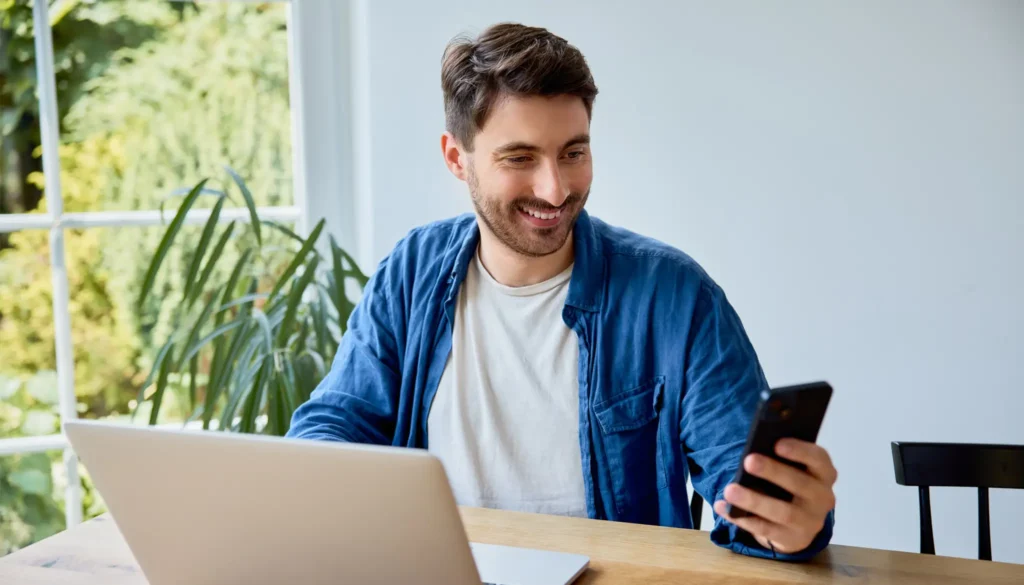 Entrepreneur heureux devant son ordinateur portable, en train de gérer son activité sur son smartphone