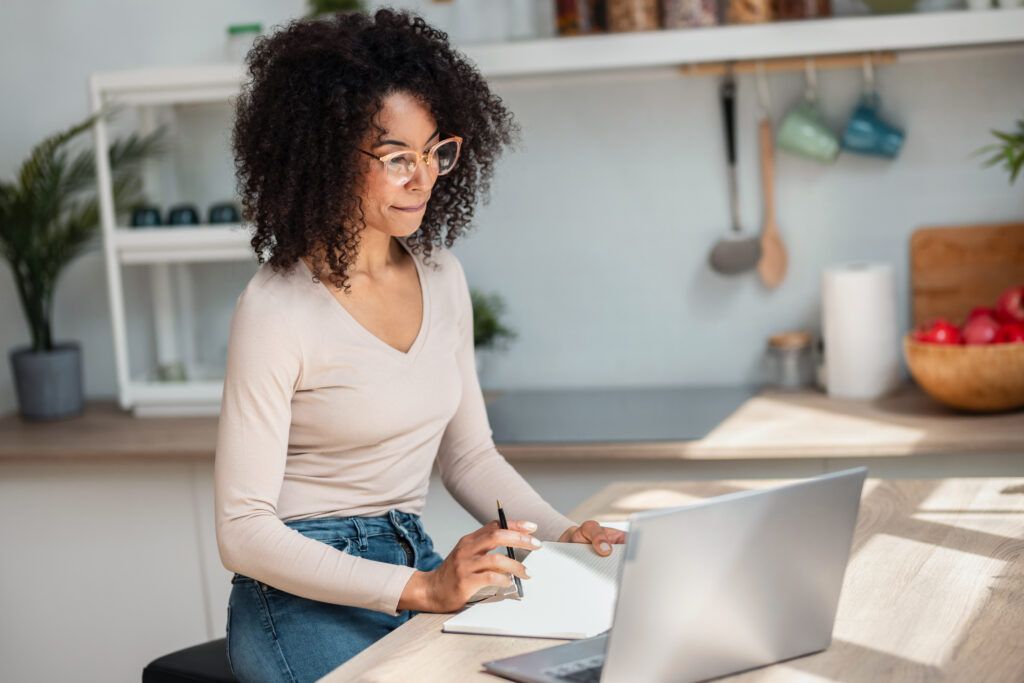 Cheerful attractive woman working with laptop in the kitchen at home.