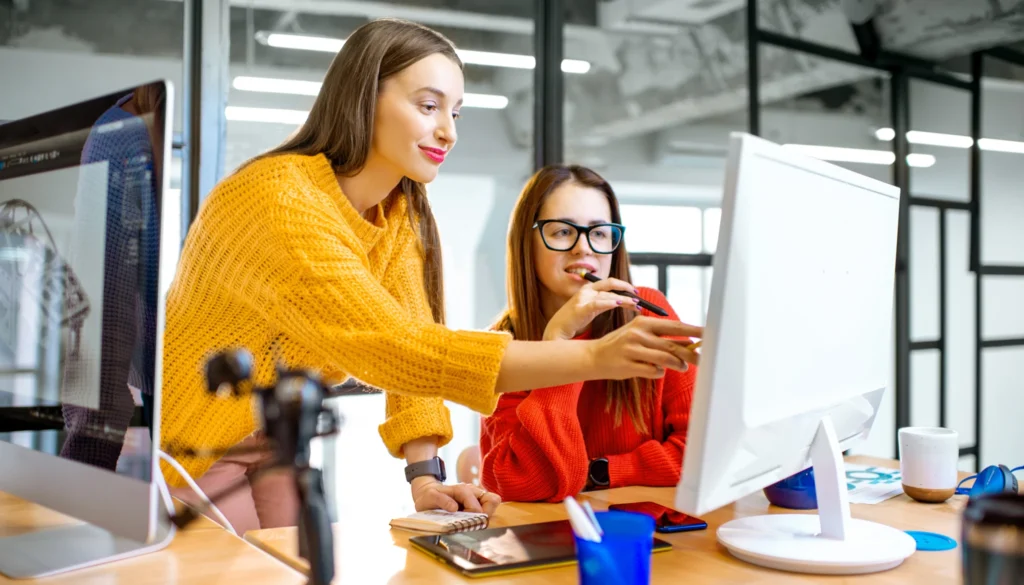 Deux jeunes femmes créatives vêtues de pulls travaillant sur ordinateur dans un bureau moderne