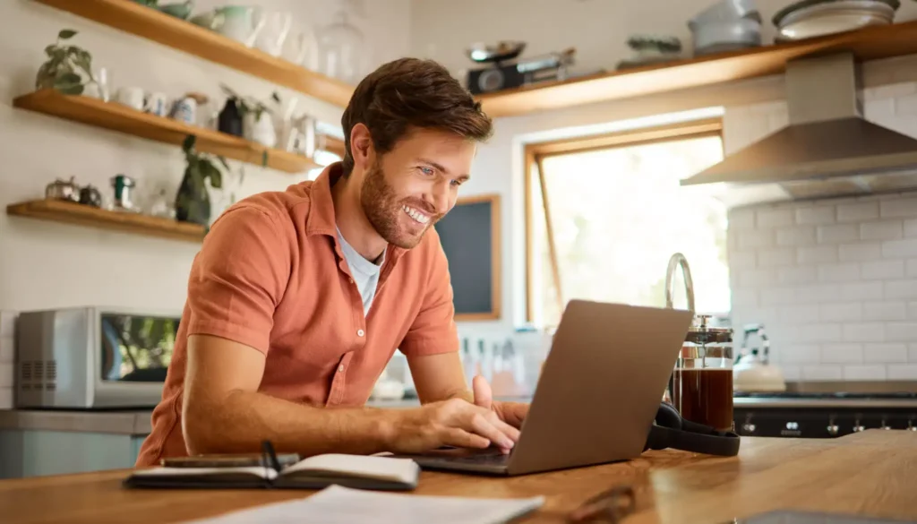 Homme souriant de profil, en home office dans sa cuisine devant son ordinateur